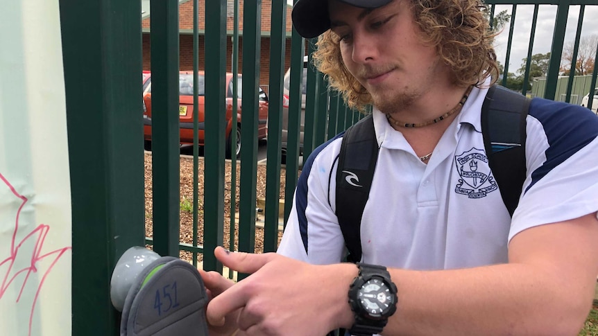 A male school student unlocks his phone from a pouch at the school gates