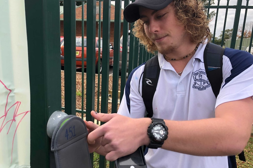 A male school student unlocks his phone from a pouch at the school gates