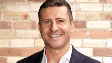 a man in a suit smiling in front of a brick wall