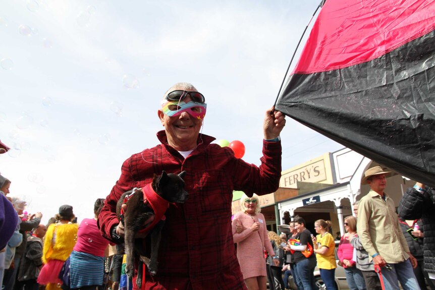 Laine marches in a LGBT parade in Broken Hill holding a small tent and dog and wearing a mask