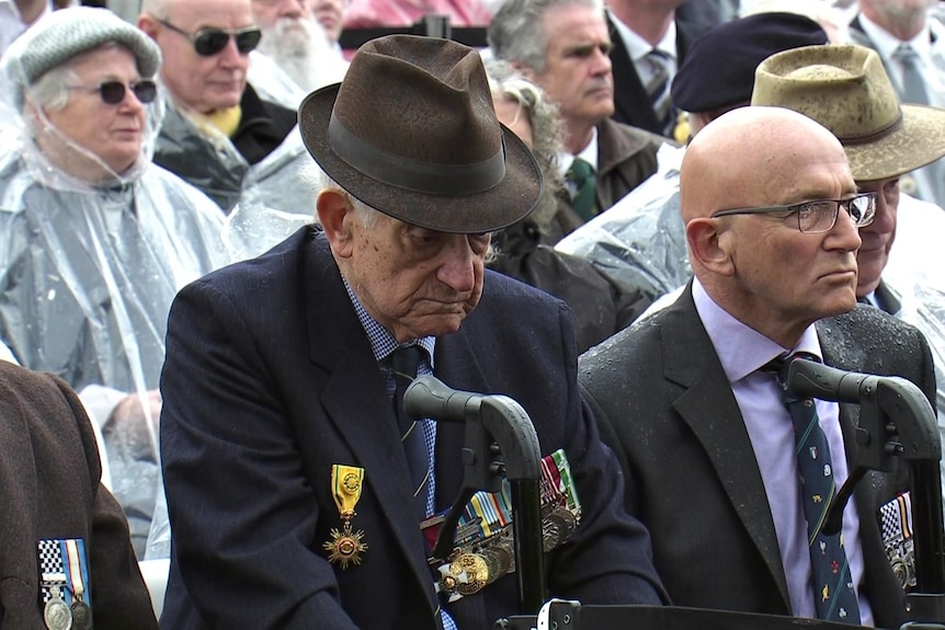 A group of men sit solemnly on chairs lined up at the service, some in uniform and wearing medals