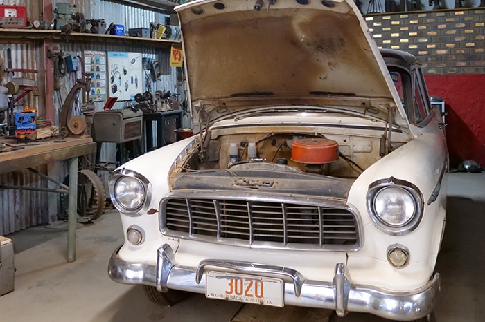 Shed with old car, hood open, car memorabilia around