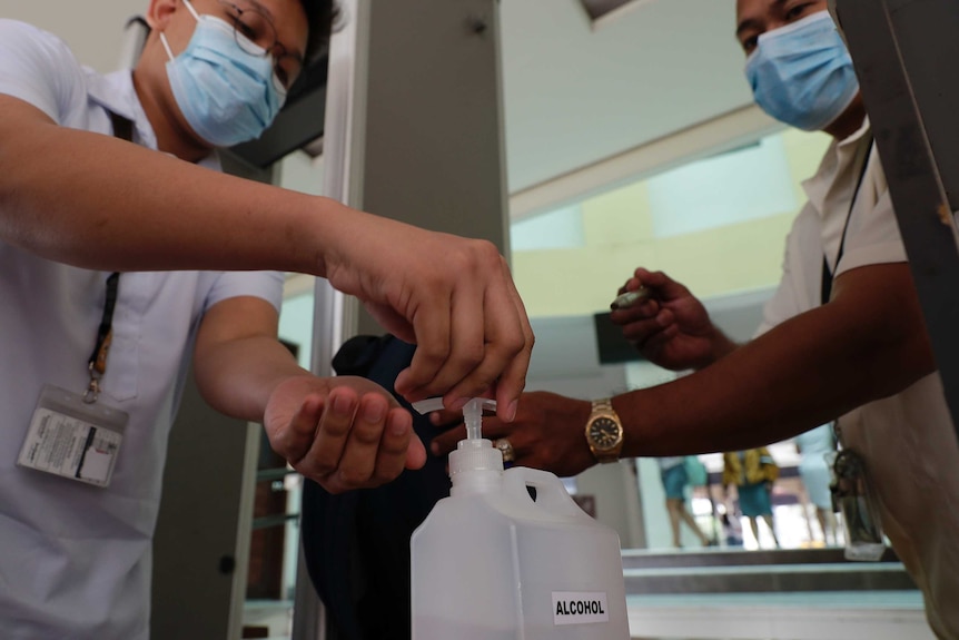 Two students wearing face masks pour alcohol on their hands.