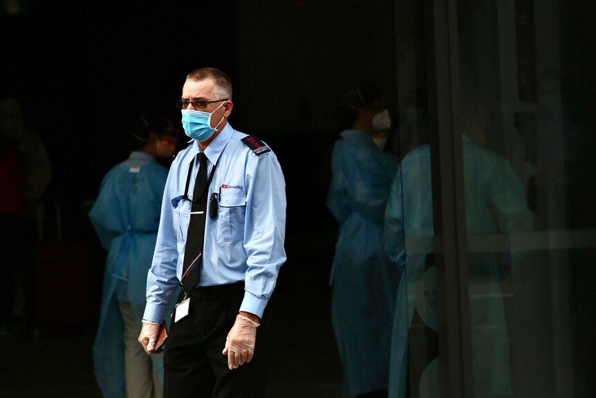 A security guard wearing a facemask, glasses and gloves stands outside the Novotel on Murray Street.