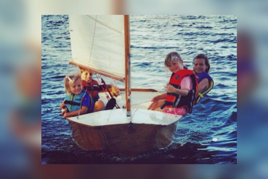 Photo from an old print showing four small children sailing in a timber boat