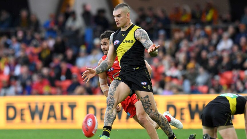 A male AFL player drops a football onto his right foot as he kicks to a teammate.