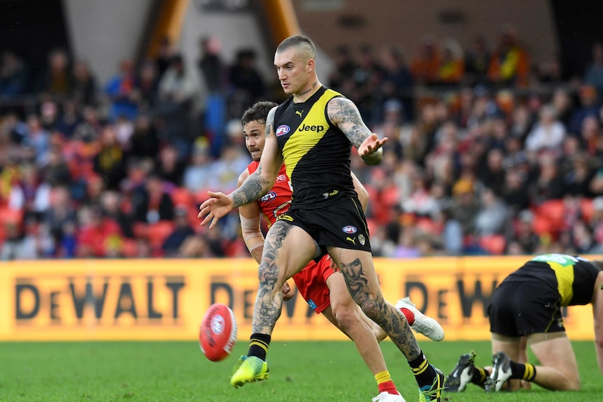 A male AFL player drops a football onto his right foot as he kicks to a teammate.