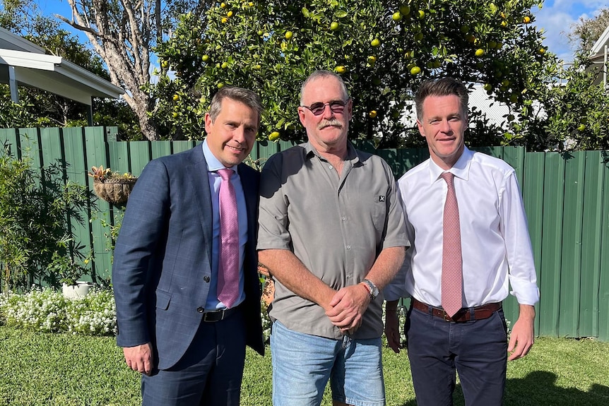 Three men – two middle aged and formally dressed and one older – standing in a backyard.