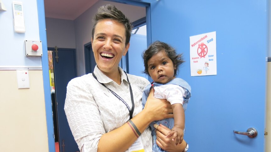 Woman with short hair beaming with a big smile and holding a baby in arms in a hospital environment