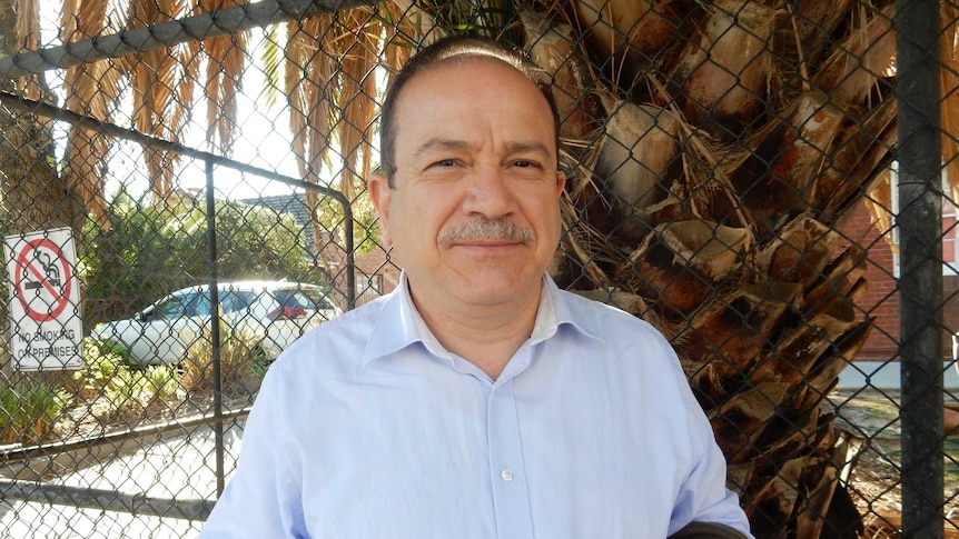 Tamer Antakly stands in front of a wire fence with a palm tree behind him