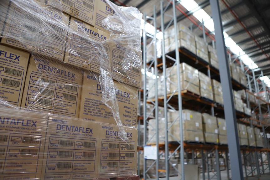 Large concrete floor warehouse with rows of boxes of medical equipment stacked high beneath a silver padded roof