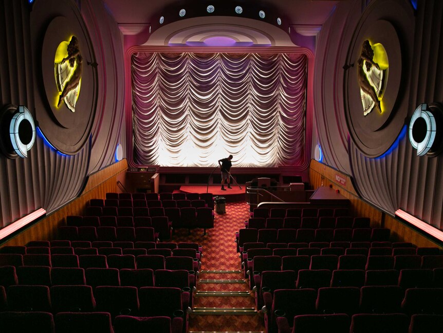 A staff member vacuums the red carpet inside the dimly-lit cinema