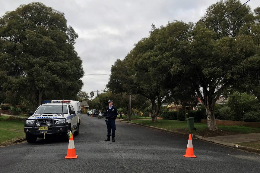 A police officer stands in front of police tape in a suburban Wagga Wagga street