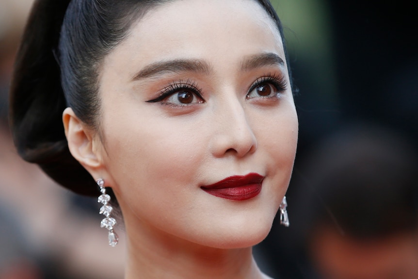 A close-up of Fan Bingbing, who is wearing a dark red lip and dangling diamond earrings