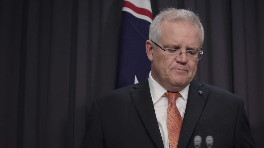 Mr Morrison is pictured right of frame, looking downwards. An Australian flag is behind him, as he stands at the lectern.