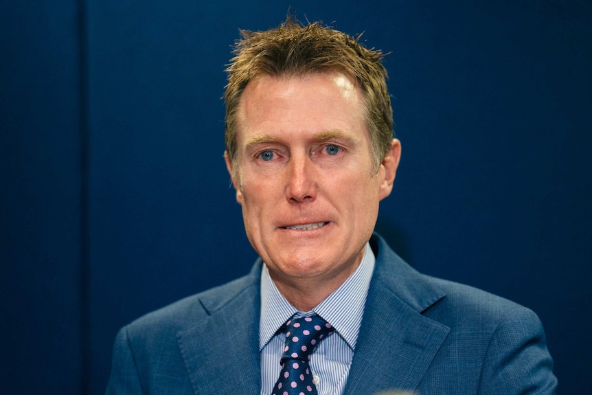 Christian Porter cries while speaking at the conference, in front of a blue background.