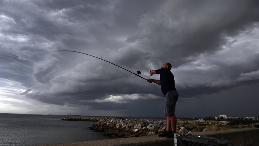 A fisherman casts his rod as storm clouds pass over Botany Bay in Sydney