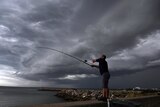 A fisherman casts his rod as storm clouds pass over Botany Bay in Sydney