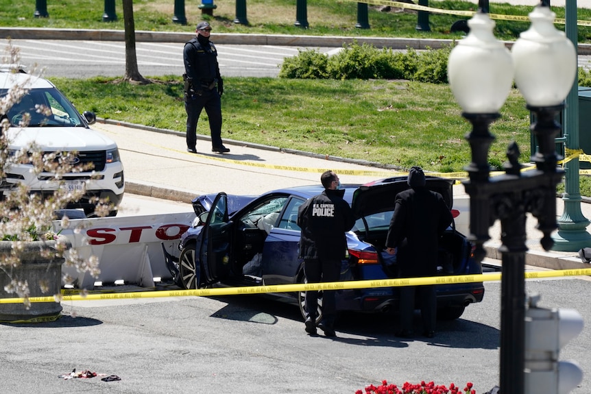 Police stand around a car that has smashed into a barrier. 