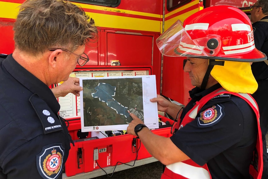 Two QFES firefighters point at a map showing where crews are on the ground.