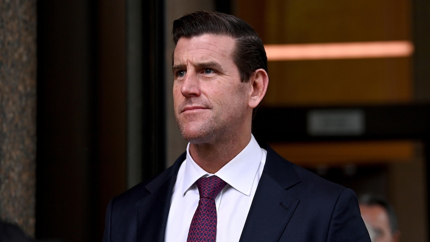 A man wearing a suit looks off to the side as he walks from court