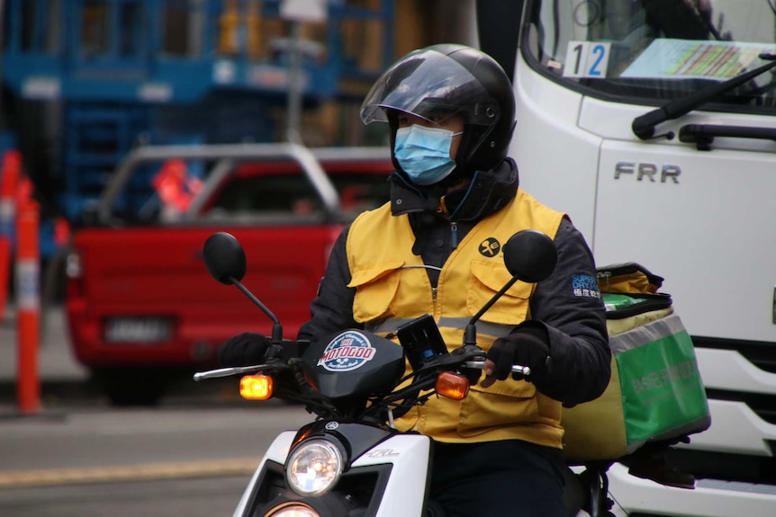 A man on a food delivery scooter wears a surgical mask