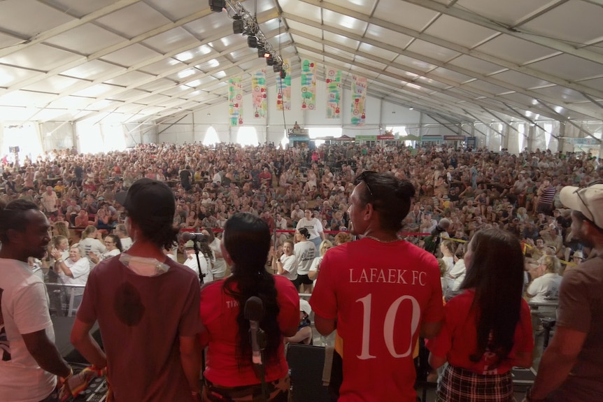 Timorese people stand on stage with a huge crowd watching in a festival tent