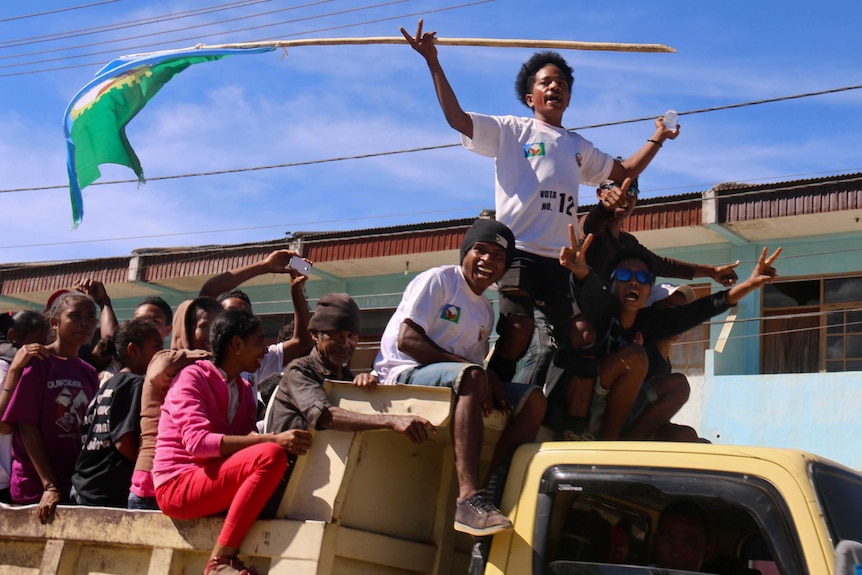 Young Timor-Leste man carrying a flag stands on a truck full with other young men.