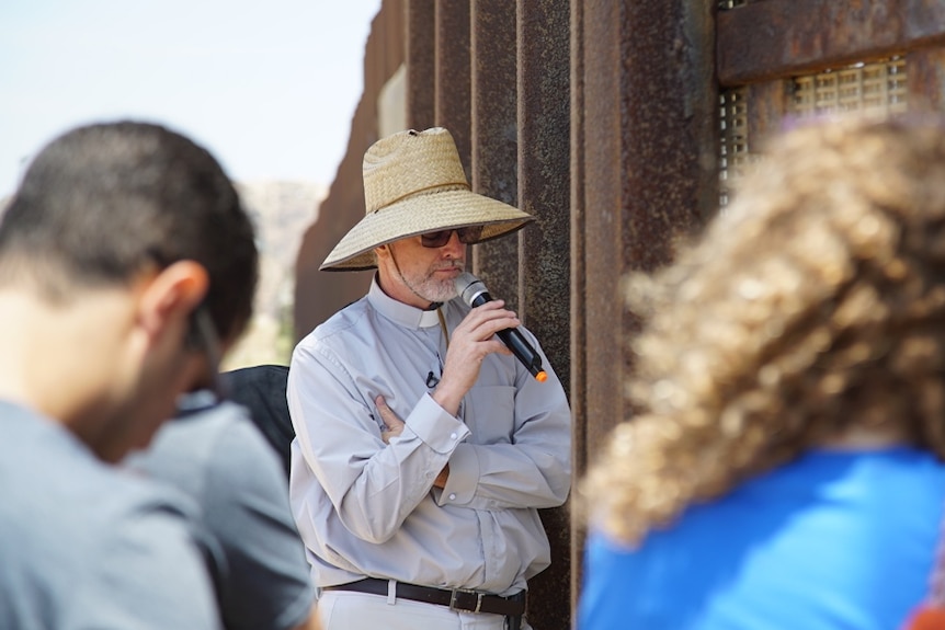 People listen as priest John Fanestil talks into a microphone at the US-Mexico border.