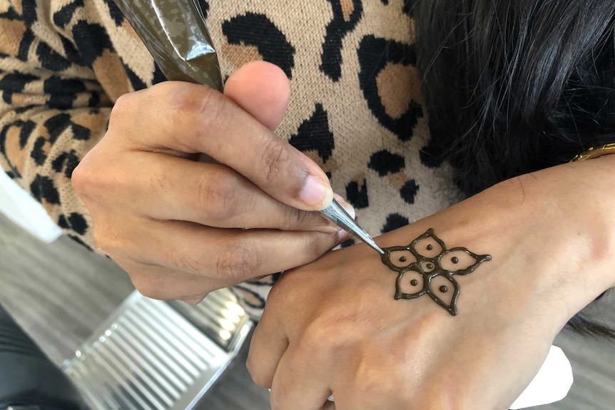 A close up image of henna being drawn onto a woman's hand.