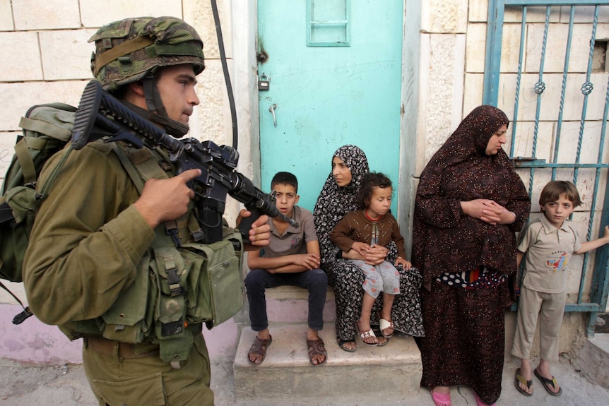 Israeli soldier walks past Palestinians