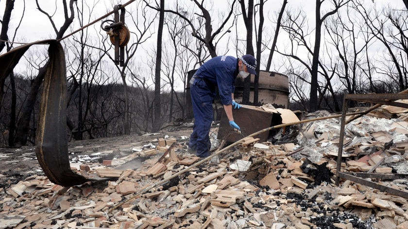 A member of a Disaster Victim Identification Team looks through remains of a burnt out house