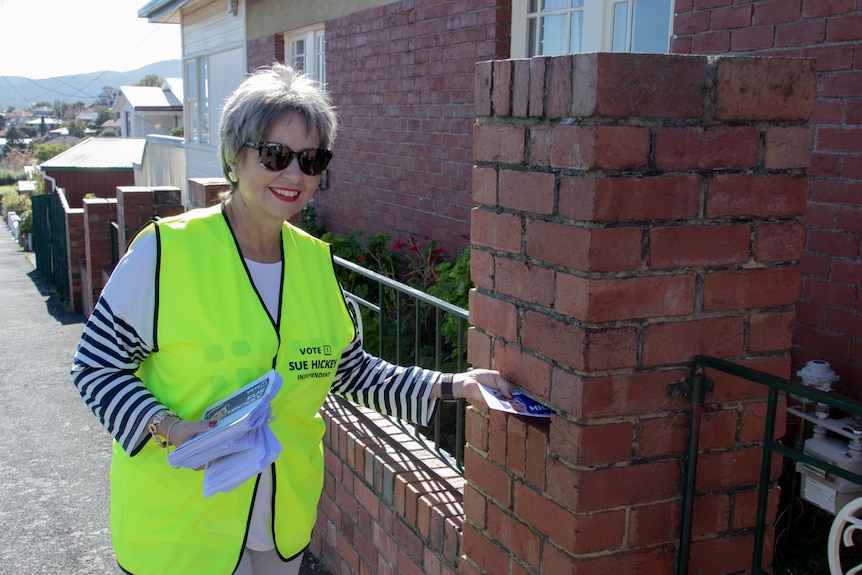 A woman with short grey hair wearing a hi-vis vest drops election campaign material in letterboxes.