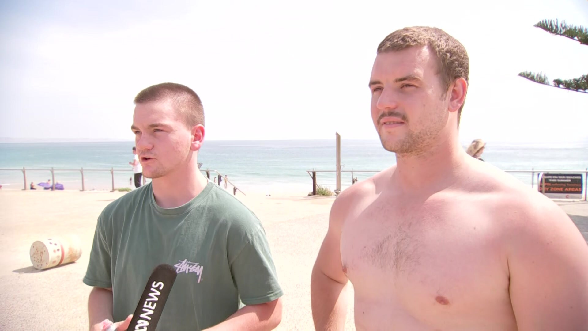 Two young men with short brown hair standing at the beach.