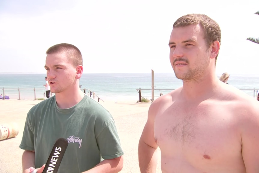 Two young men with short brown hair standing at the beach.