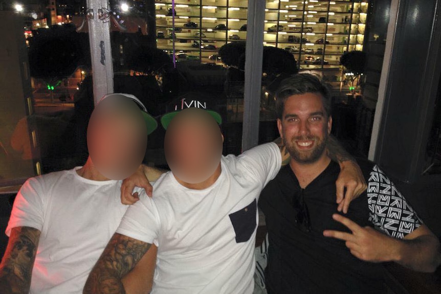A photo taken from Facebook shows Andrew Morrison posing with two friends whose faces have been blurred out.