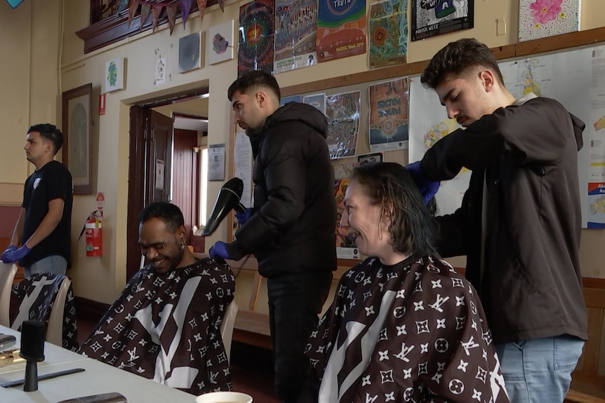 Two people laughing while getting their hair cut by two hairdressers.