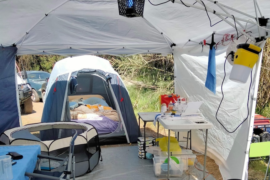 The inside of  a gazebo with a tent and bedding in the background.