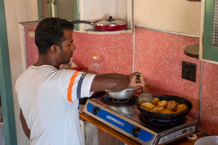 A man cooks chicken on a stove in a run-down house.