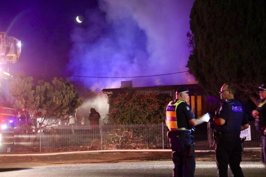 Two policemen stand in front of a building, with billowing purple smoke going into the sky.