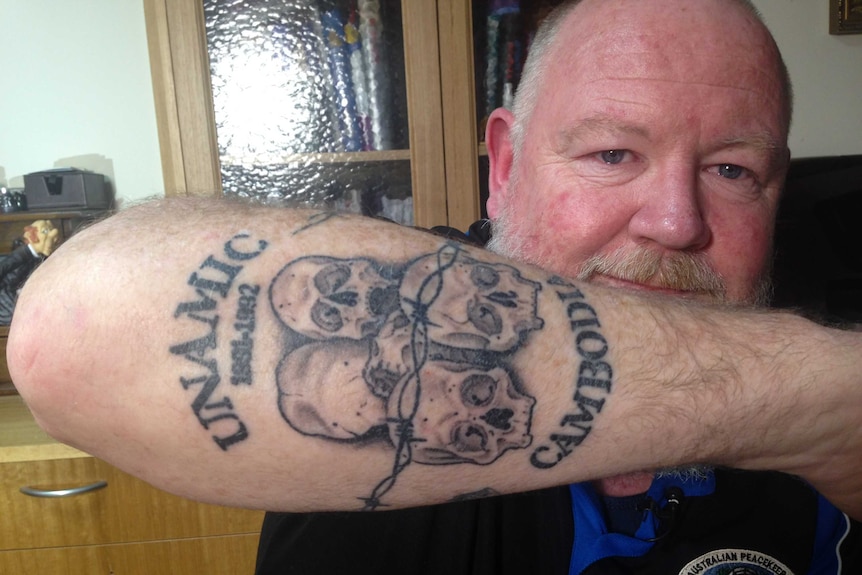 Mike Quinn holds up his forearm, showing the camera a tattoo of skulls.