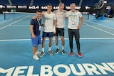 Four men on a tennis court pose for a picture.
