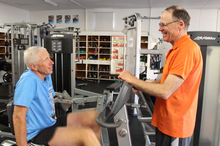 Two middle-aged men at a gym working with the equipment