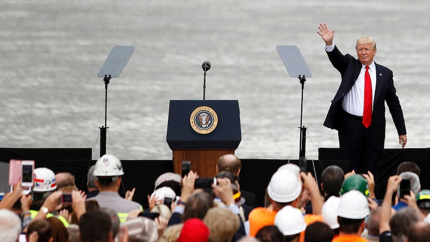 US President Donald Trump waves to a crowd of people wearing hard hats.