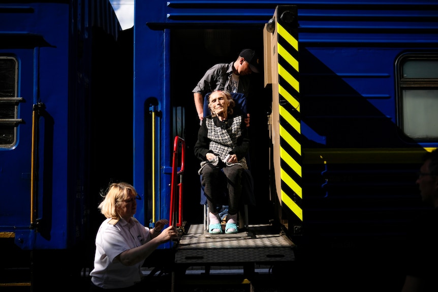 a woman looks out from a train after being helped to board by people using a wheelchair
