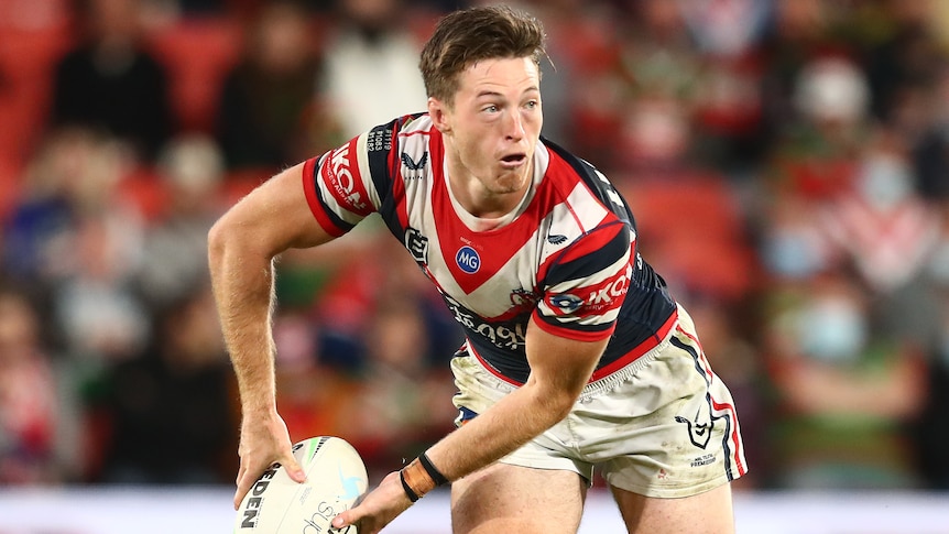 A Sydney Roosters NRL player holds the ball as he prepares to pass to his left.