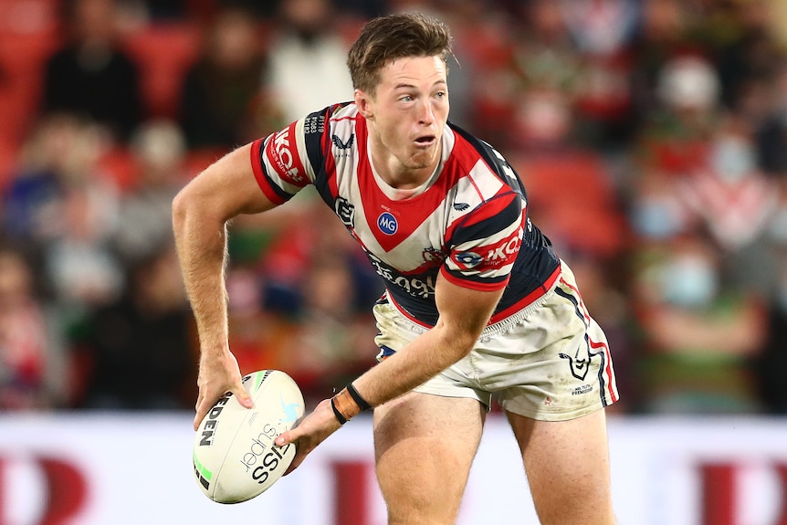 A Sydney Roosters NRL player holds the ball as he prepares to pass to his left.