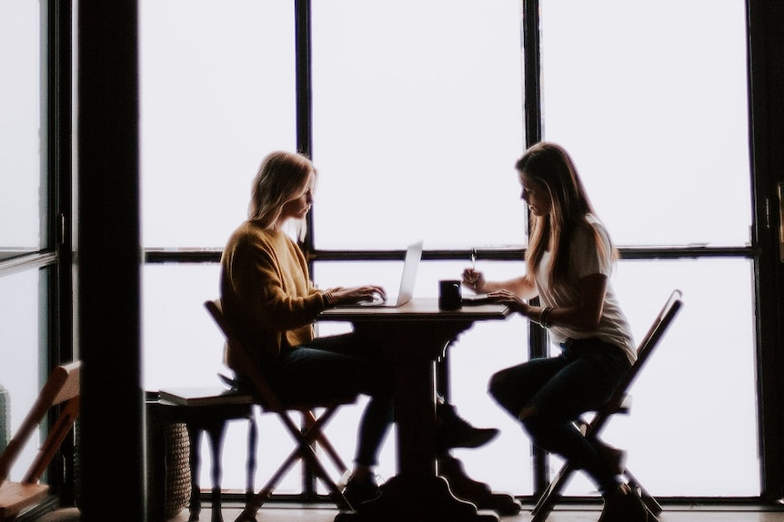 Two women work at a table for a story about lending money to friends