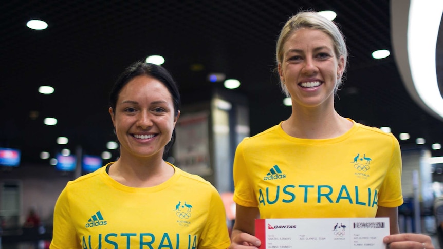 Kyah Simon and Alanna Kennedy stand holding Qantas boarding passes in team Australia kit