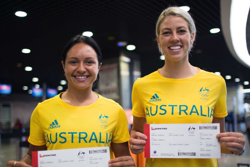 Kyah Simon and Alanna Kennedy stand holding Qantas boarding passes in team Australia kit